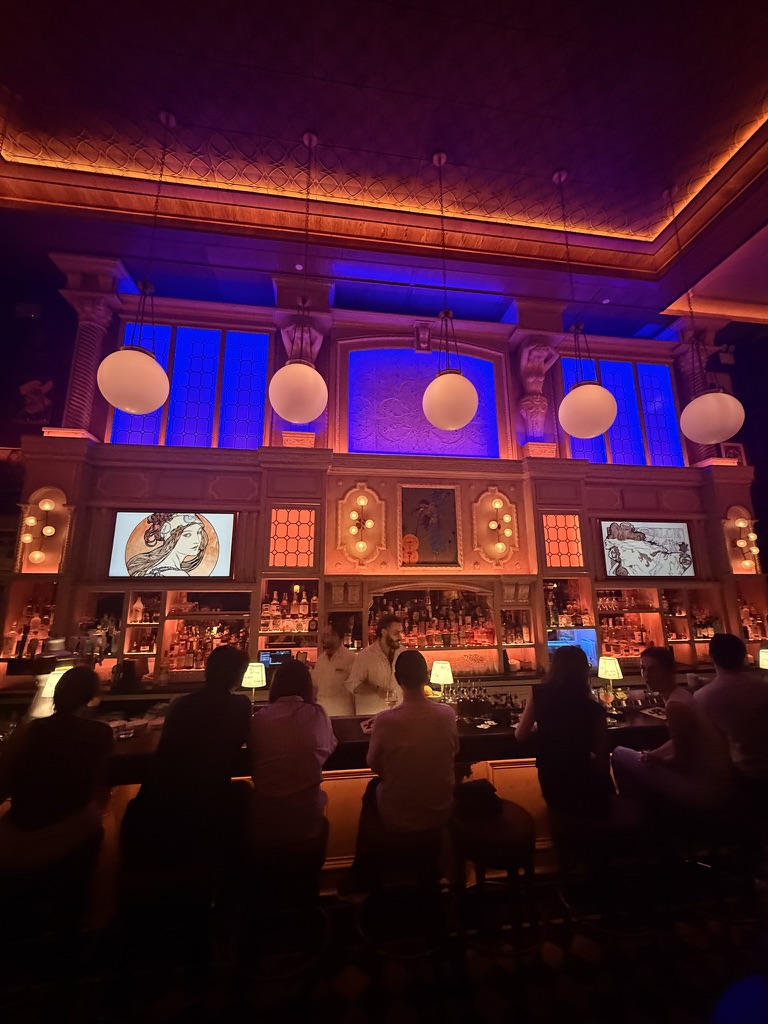 Bar Lola in New York City, with guests at an amber-lit bar beneath blue and violet glass panels