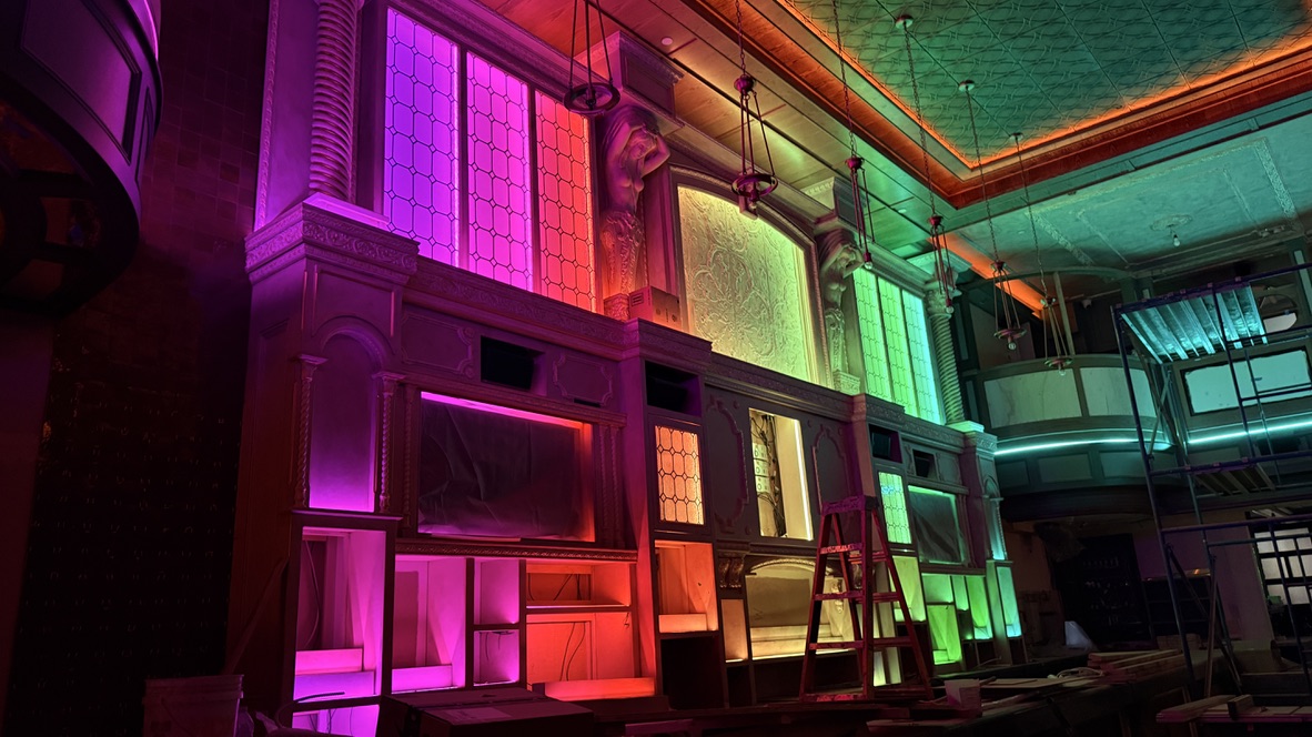 Bar Lola during installation, with magenta, red and green lighting across the back bar and a ladder in place